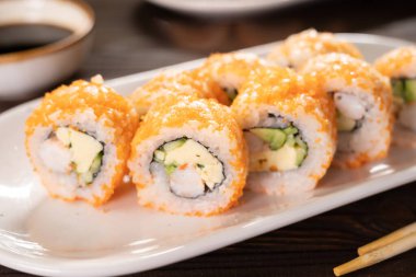 Suşi seti, karides, uçan balık reo, avokado ve beyaz tabakta salatalık. Japon mutfağı kavramı