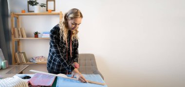 Güzel bir kadın cetvelle kumaşa desenler çiziyor, ev içinde el yapımı kıyafetler yapıyor. Yaratıcı beceri tasarımı. hobiler ve yaşam tarzı konsepti