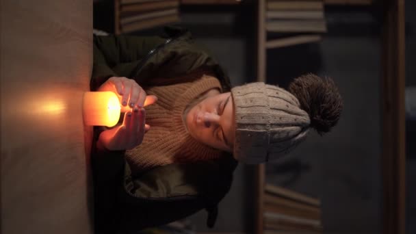 穿着冬衣的冻僵的年轻女子在灯光下用蜡烛取暖 在欧洲造成停电的能源危机期间 没有暖气 也没有电 垂直录像 — 图库视频影像