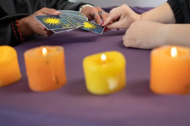 Falcı elinde tarot kartları ve mum ışığında yanan mumların yanındaki masada kart seçiyor..