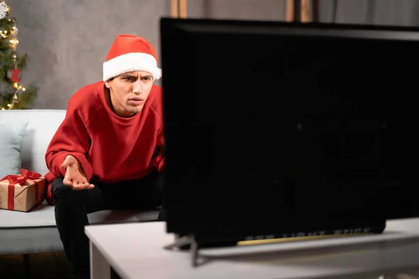 Genç Yakışıklı Adam Evdeki Kanepede Televizyon Izliyor Noel Baba Şapkalı — Stok fotoğraf