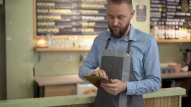 Kafede dikilirken elinde dijital tablet tutan neşeli sakallı genç bir erkek. Küçük işletme kavramı