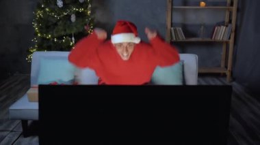Noel Baba şapkalı heyecanlı bir futbol fanatiği koltukta oturuyor ve Noel için dekore edilmiş bir odada televizyonda maç izliyor. Şampiyonluğu kazan..