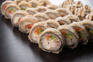 Tempura Maki siyah arka planda takılıyor. Somon, yengeç ve salatalıklı sıcak suşi. Modern Japon menü konsepti.