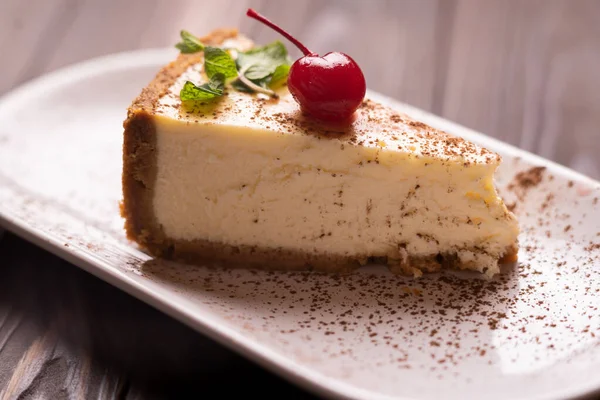 Cheesecake dilimi, New York tarzı klasik peynirli kek beyaz tabakta, ahşap arka planda. Restoran menüsü tatlı konsepti