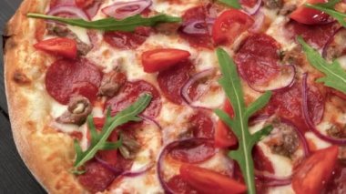 Ahşap bir masada pepperoni domatesli ve roka aromalı lezzetli pizza. İtalyan restoran menüsü konsepti. Kapat.