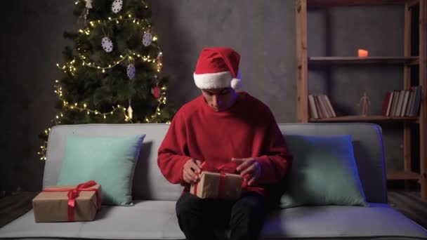 크리스마스 모자를 남자가 상자를 소파에 크리스마스 크리스마스 크리스마스 트리등에 포장을 — 비디오
