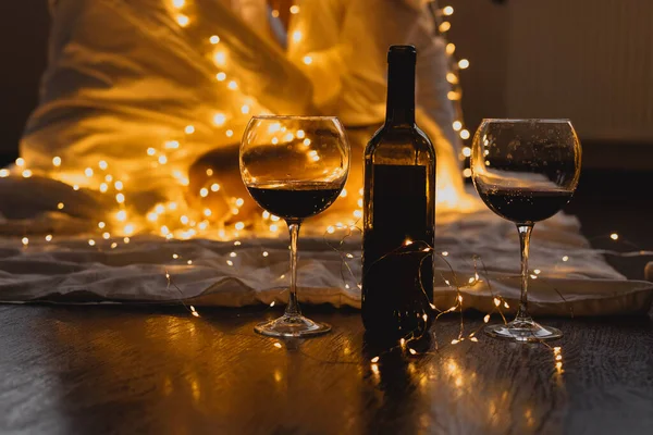 Romantic evening at home a bottle of wine and two glasses, a garland and a festive mood, valentine\'s day celebration concept