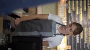 Kahveci tezgahında gülümseyen garson bayan garson, kadın müşterisi cep telefonu ödemesi yapmak için NFC terminali kullanıyor. Dikey video