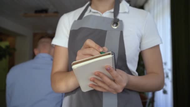 贴身女服务员穿着围裙站在咖啡店 女咖啡店工作人员拿着笔记本等着 准备接客人 客人在餐馆点菜 招待费 — 图库视频影像