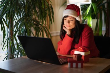 Noel Baba şapkalı üzgün hippi kadın Noel zamanı evde oturuyor. Zor bir gündü. Sanal Noel partisi. Boşluğu kopyala