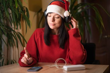 Hippi kadın evde müzik dinliyor. Noel hanımefendisi telefonu modern teknolojiyle dinleyip radyo kulaklığı melodisi dinliyor. Boşluğu kopyala