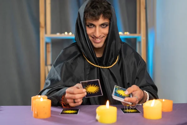 Man fortune teller reading the future by tarot cards sitting at a table with candles. Copy space