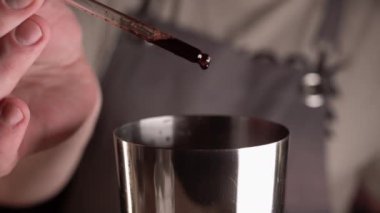 Barmen tezgahta kokteyl hazırlıyor. Sallanan pipetli acı bir sıvı ekliyor. Kapat.