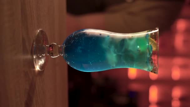 バーの暗い背景にアルコールカクテルブルーラグーンのガラス 垂直ビデオ — ストック動画
