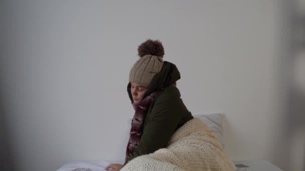 冬天醒来的年轻女子穿着保暖的衣服 躺在冰冷 没有暖气的房子里 破产的穷人无力支付电费 战后的生活 无热能 能源危机概念 — 图库视频影像
