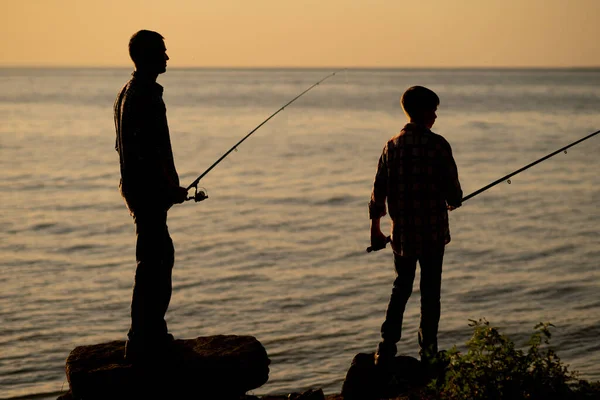 Silhouette of father and son fishing at sunset in summer on the sea. Copy space
