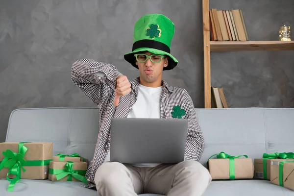 Man on sofa using laptop doing online shopping showing thumbs down bad online store service dissatisfied customer shopping for St. Patrick\'s Day. Copy space