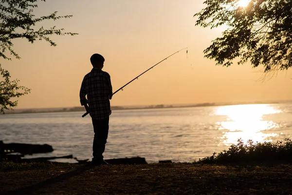 Silhouette of a boy fishing on a lake in the summer at sunset. Copy space