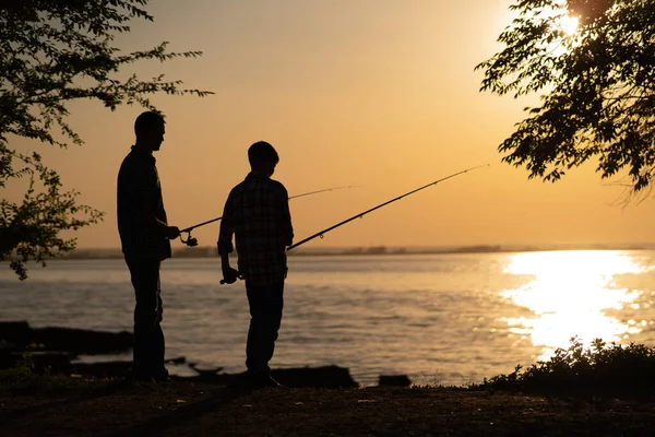 silhouette of man and teen boy fishing on the lake. Copy space