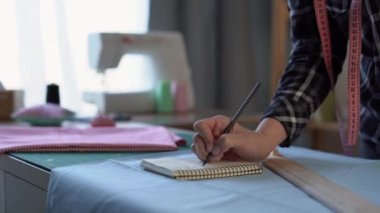 Kadın moda tasarımcısının ölçü alıp not defterine yazdığına yakın çekim. Yüzsüz