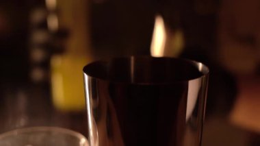 Barmenlerin ellerinin bardaki metal karıştırıcıya alkol ve meyve suyu döktüğü yakın plan..