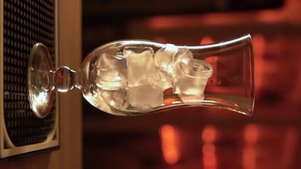暗い背景に木製のバーカウンターの上に空のカクテルガラスの氷のキューブ 垂直ビデオ — ストック動画