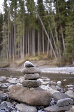 Few stacked stones next to a river with forest on background. Copy space
