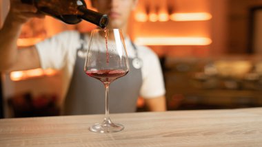 Bartender pouring red wine into a glass, close up. Hospitality and beverage concept. Copy space