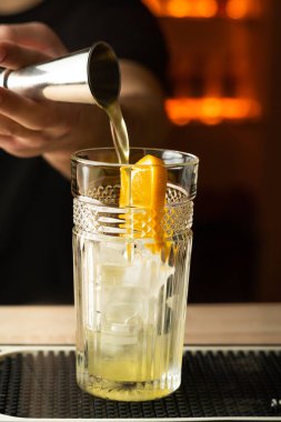 Barman pouring alcoholic drink into the glass with ice cubes on the bar counter. Copy space