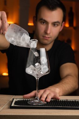 Barman pouring ice cubes into the cocktail glass making a alcoholic cocktail. Copy space