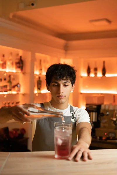Bartender pouring tonic water in alcoholic cocktail in glass on bar counter. Copy space