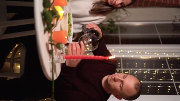 恋爱中的快乐夫妻在家里或餐馆庆祝情人节 与蜡烛约会 男人倒红酒坐在浪漫的餐桌旁 2月14日庆祝情人节 垂直方向 — 图库视频影像