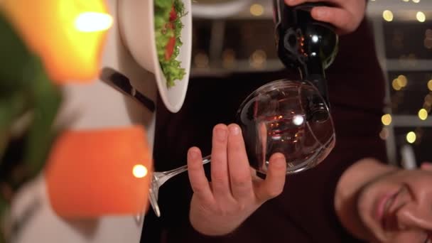 恋爱中的快乐夫妻在家里或餐馆庆祝情人节 他们与蜡烛约会 男人在浪漫的餐桌边倒红酒 2月14日 情人节 垂直录像 — 图库视频影像