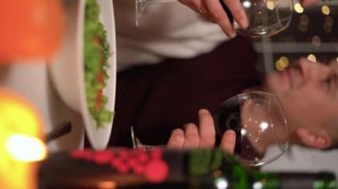 Aşık mutlu çift sevgililer gününü evde ya da restoranda yemek yiyerek, kırmızı şarap içerek romantik masada oturarak kutluyor, kapatıyorlar. 14 Şubat Sevgililer Günü. Dikey video.