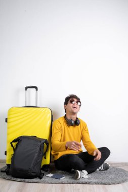 Traveler tourist man wear sweater sitting near suitcase look up isolated on plain white background studio. Air flight journey concept