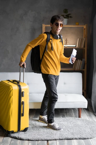 Positive traveler man with luggage yellow suitcase leaving his home. Copy space