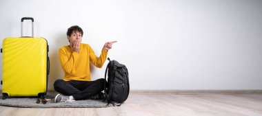 Bavullu gezgin, ağzı yanlışlıkla ellerle kaplayan şok olmuş, parmaklarını beyaz arka planda yalnız gezen yolcu hafta sonları yurtdışına seyahat ederken gösteriyor. Hava yolculuğu