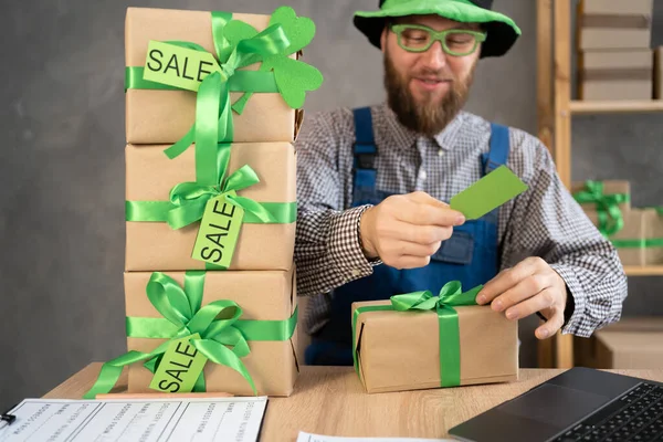 Small business owner with laptop and gift boxes with sale tags on table in home warehouse. Online ecommerce retail business St.Patricks Day discounts deals, free shipping. Best buy holiday offers