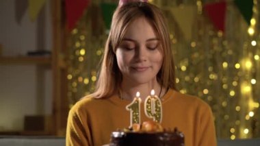 19. yaş günü. Doğum günü pastasına mum üfleyen genç bir kadın. Kek tutarken dilek tutan bir kız