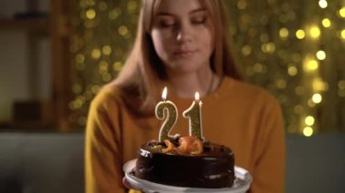 21. yaş günü. Doğum günü pastasında mum üfleyen genç bir kadın. Lezzetli bir pastayı tutarken dilek tutan kız.