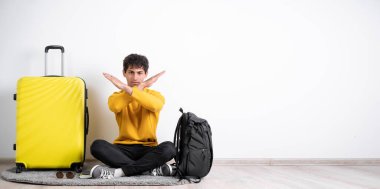 Elinde bavulla oturan gezgin adam izole edilmiş beyaz arka plan reddedilme ifadesi kollarını kavuşturarak negatif işaret yapıyor, hayır, kızgın surat. Boşluğu kopyala