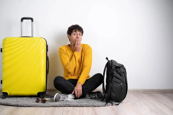 Worried traveler tourist man in sweater with suitcase sit, hand palm covering mouth, confidential info isolated on white background Passenger travel abroad weekends getaway. Air flight journey concept