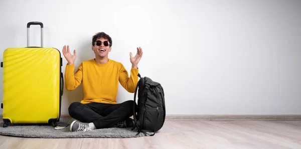 Full height traveler tourist man in sweater with suitcase sit, happy expression and raising arms isolated on white background Passenger travel abroad weekends getaway. Air flight journey concept