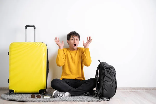 shocked traveler young man in sweater and with suitcase screaming and touching face with surprised expression face, over isolated white background. Banner