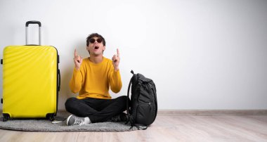 Uzun boylu, bavullu turist oturur, parmaklarıyla beyaz arka planda izole edilmiş yönleri işaret ederek hafta sonları yurtdışına seyahat eder. Hava yolculuğu