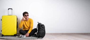 Genç Arap turist, izole edilmiş beyaz arka planda oturmuş gülümsüyor ve telefonda konuşuyor. Ara beni. Hava yolculuğu konsepti