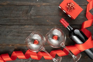 Sevgililer günü kartı, şarap şişesi, kırmızı hediye ve ahşap arka planda iki bardak. Yukarıdan bak. Boşluğu kopyala.