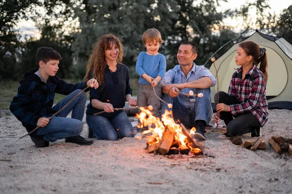Happy family roasting marshmallow over campfire in the evening. camping, travel, tourism, hike and people concept