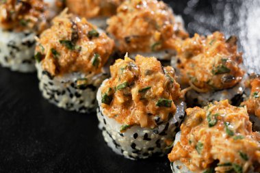 Somon, avokado, midye ve siyah susam tohumlu taze suşi ruloları siyah bir taş levhada servis edilir. Japon suşi uramaki ya da California dürümü. Kapat.